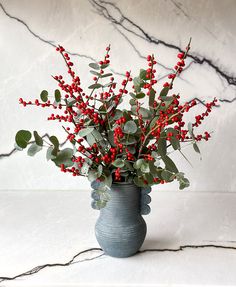 a vase filled with red berries and greenery on top of a white countertop