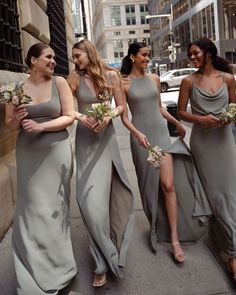 four bridesmaids walking down the street in their gray dresses and holding bouquets