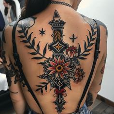 the back of a woman's tattoo with an ornate cross and flowers on it