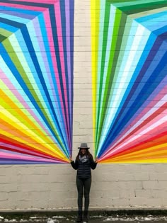 a woman standing in front of a wall with large rainbow colored beams painted on it