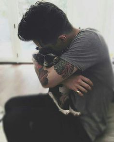 a man with tattoos on his arm hugging another man's neck and shoulder while he is sitting down