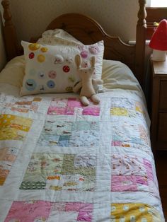 a small child's bed with a quilt and stuffed animal on the pillow in front of it