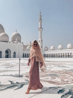 a woman in a hijab walks through the courtyard of a white building with arches and domes