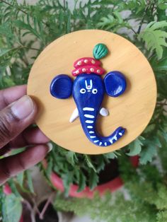 a hand holding up a wooden plaque with an elephant painted on it