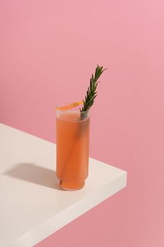 a drink with an orange garnish in it on a pink and white table