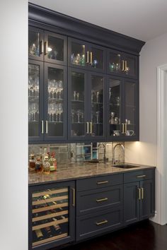 a kitchen with black cabinets and marble counter tops, wine glasses on the glass doors