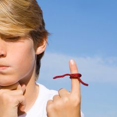 a young boy is pointing to the red string on his finger that he has placed in front of him