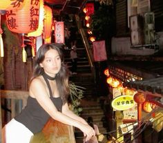 a woman riding a bike down a street next to chinese lanterns and stairs at night