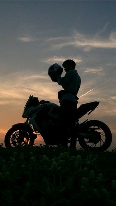 a man sitting on top of a motorcycle next to a field full of flowers at sunset