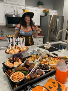 a woman in a halloween costume standing next to a table full of food and treats