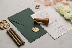 the wedding stationery is laid out on top of an envelope and some gold buttons