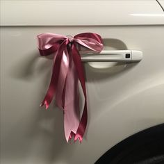 a white car with a pink ribbon tied to it's door handle and on the side