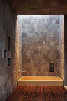 a wooden floor in front of a stone wall with a bathtub on one side