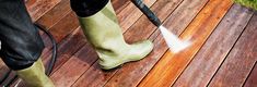 a person in rain boots is using a pressure washer to clean a wooden deck