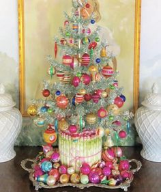 a small christmas tree with ornaments on it in front of a painting and vases