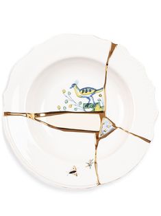 a broken white plate with gold trimmings and a blue bird on it's side