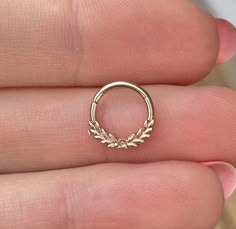 a gold nose ring with leaves on the side and an arrow in the middle, sitting on someone's finger