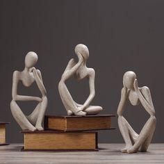 three statues sitting on top of books in front of a gray background and one is holding his head