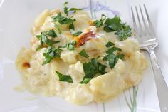 a white plate topped with macaroni and cheese covered in parsley next to a fork