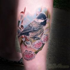 a bird sitting on top of a branch next to a person's leg with flowers around it