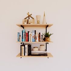 three wooden shelves with books, vases and other decorative items on them against a white wall