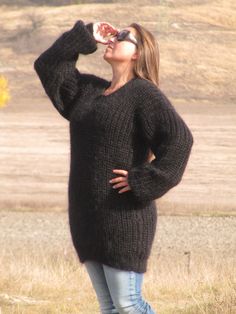 a woman standing in a field drinking from a bottle