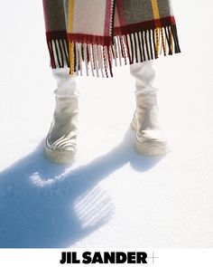 a person standing in the snow with their feet up wearing white shoes and a plaid blanket