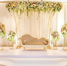 a couch sitting in front of a white stage with flowers on it and gold stands