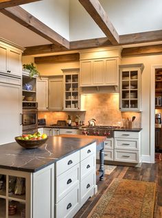 a large kitchen with white cabinets and wooden beams on the ceiling, along with an area rug that matches the hardwood flooring