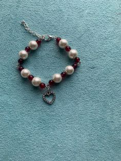 a bracelet with pearls and red beads on a blue surface, the bead has a heart charm hanging from it