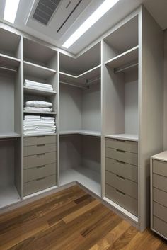 an empty walk in closet with white linens on the shelves and wooden flooring