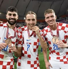 three men in red and white soccer uniforms holding their medals while standing next to each other