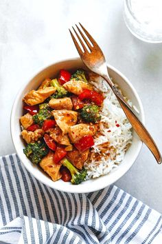 a white bowl filled with rice, broccoli and chicken next to a fork