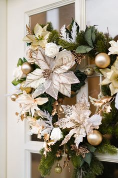 a christmas wreath hanging on the front door with gold ornaments and poinsettis