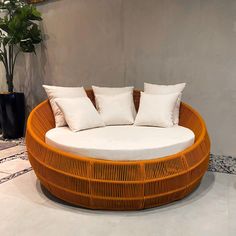 a round bed with white pillows on top of it in front of a wall and potted plant