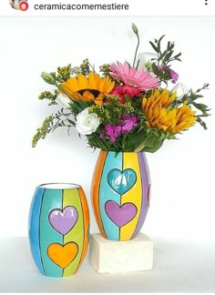 two colorful vases with flowers in them sitting on a white table next to each other