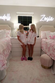 two young women standing next to each other in a room with pink bedspreads