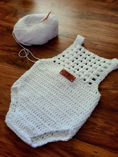 a white crochet baby romper next to a ball of yarn on the floor