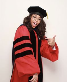 a woman in a graduation cap and gown gives the thumbs up while standing against a white wall