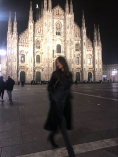 a woman walking in front of a cathedral at night