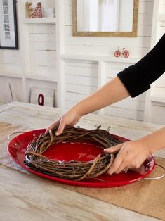 a woman is making a wreath out of twigs on a red platter with scissors