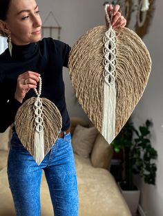 the woman is holding two large straw bags with tassels on them, and wearing blue jeans