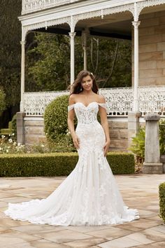 a woman in a white wedding dress standing on a brick patio with hedges and bushes