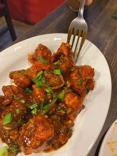 a white plate topped with meat covered in sauce and garnished with green onions