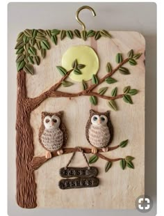 two owls sitting on a tree branch with a sign hanging from it's side