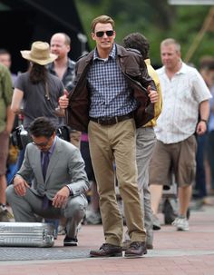 a man in a suit and tie standing next to a suitcase on the ground with other people around him