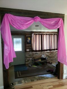 a living room with pink drapes on the ceiling and wooden floors in front of it