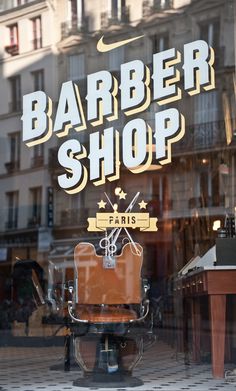 a barber shop window with an old fashioned chair in the foreground and a sign that says barber shop