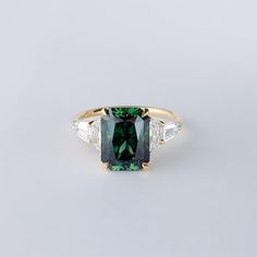 a green and white diamond ring with three baguettes on the side, set in yellow gold