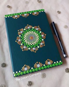 a blue notebook with green and white designs on it next to a black ballpoint pen